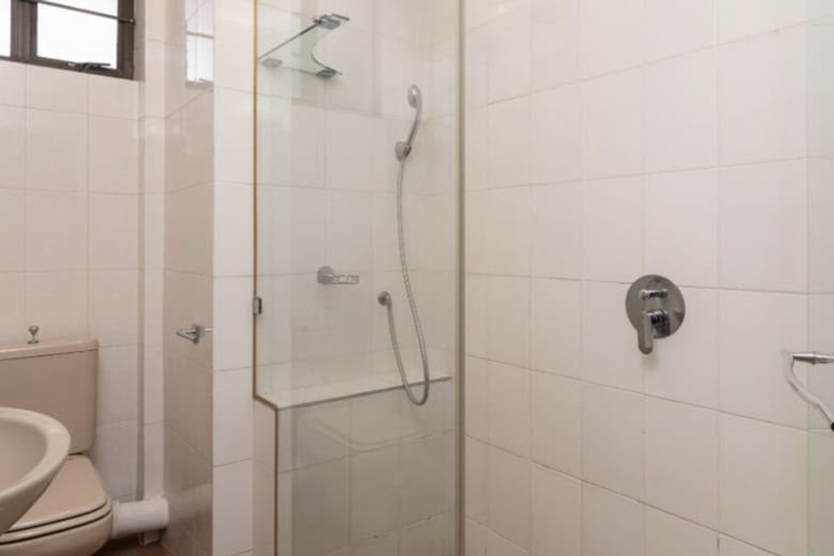 A functional bathroom featuring a glass-enclosed shower, pedestal basin, and toilet with neutral wall tiling.