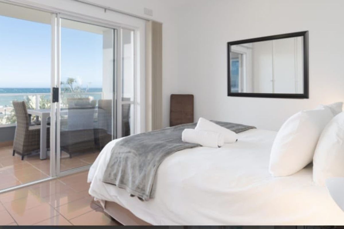 Bright bedroom featuring sliding glass doors that open onto a private balcony with ocean views and built-in storage.