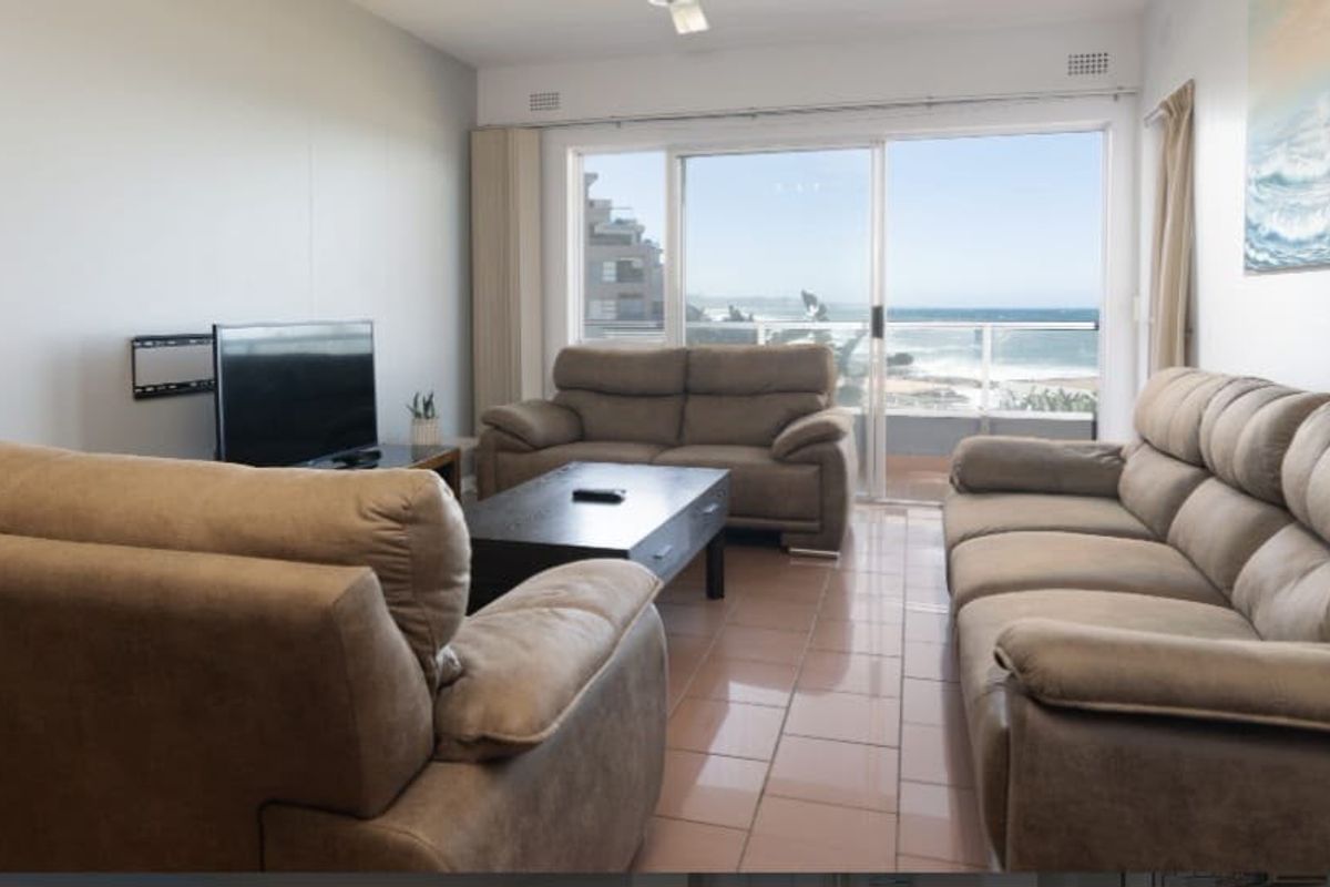 Spacious living room featuring tiled flooring and a large sliding glass door that opens to a balcony with ocean views.