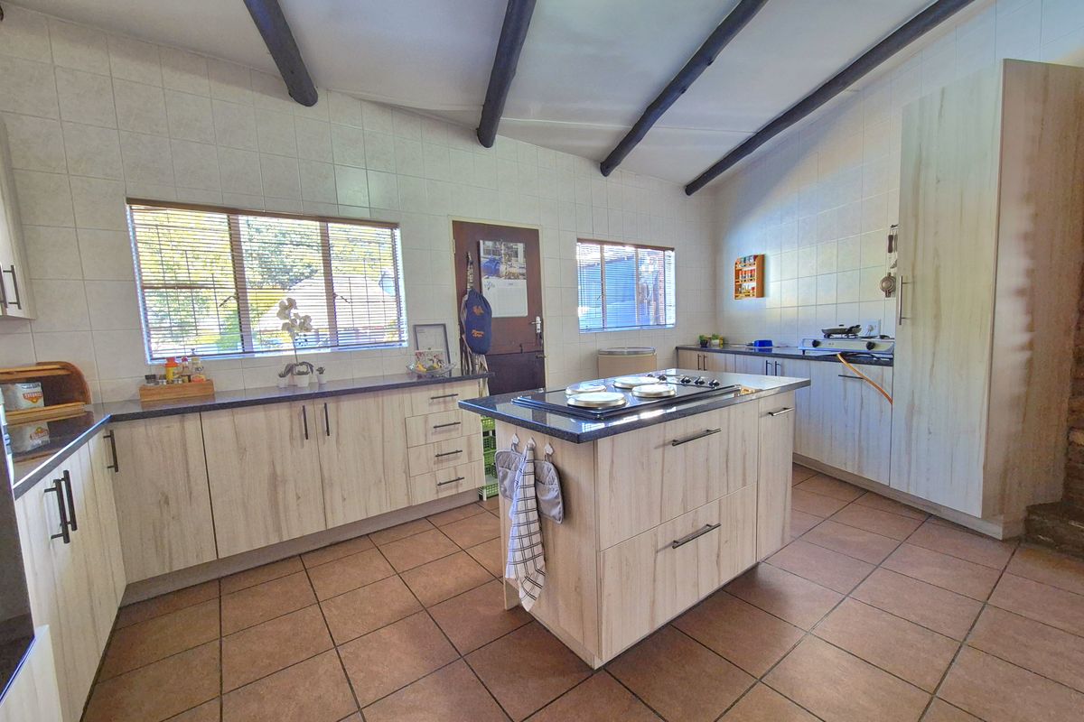 Spacious kitchen featuring a central island with a gas hob, light wood-finish cabinetry, tiled flooring, and exposed ceiling beams.
