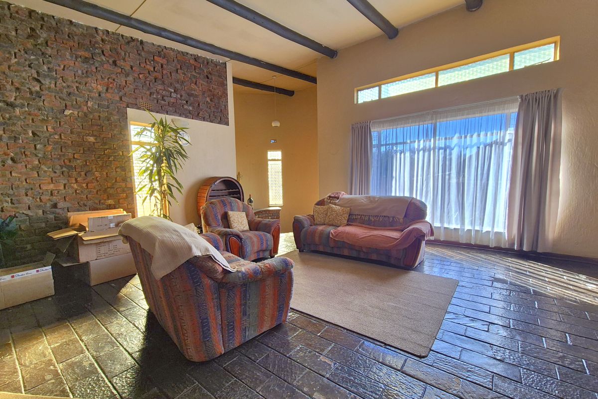 Spacious living room featuring exposed brick walls, timber ceiling beams, and large windows that provide ample natural light.