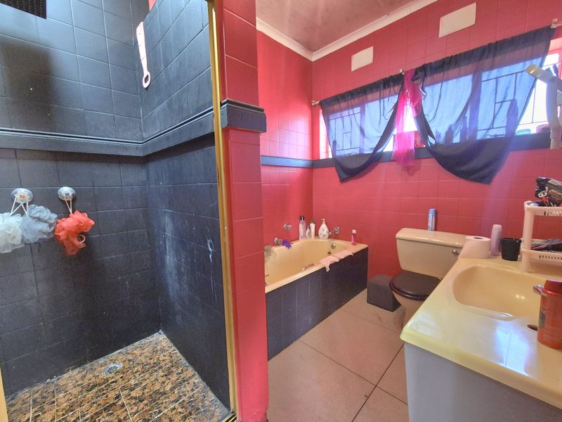 A dated bathroom featuring a separate shower enclosure, built-in bathtub, vanity basin, and toilet with bold red and black wall tiling.