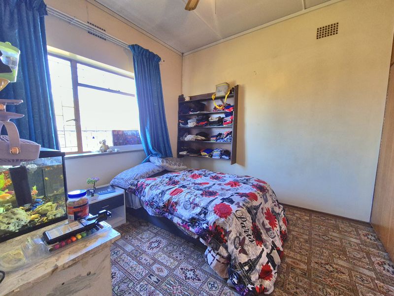 A bedroom featuring a built-in cupboard, ceiling fan, and large window. The room requires cosmetic updates to the flooring and wall finishes.