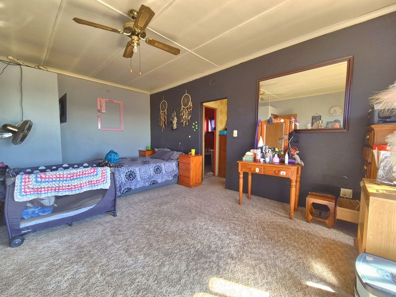 A spacious bedroom featuring a ceiling fan, wall-to-wall carpeting, and a large wall-mounted mirror, offering a functional layout with potential for cosmetic updates.