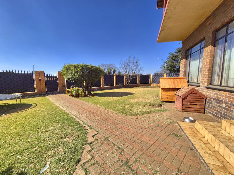A rear garden area featuring a brick boundary wall, metal security gate, paved walkway, and tiled steps leading to the house.