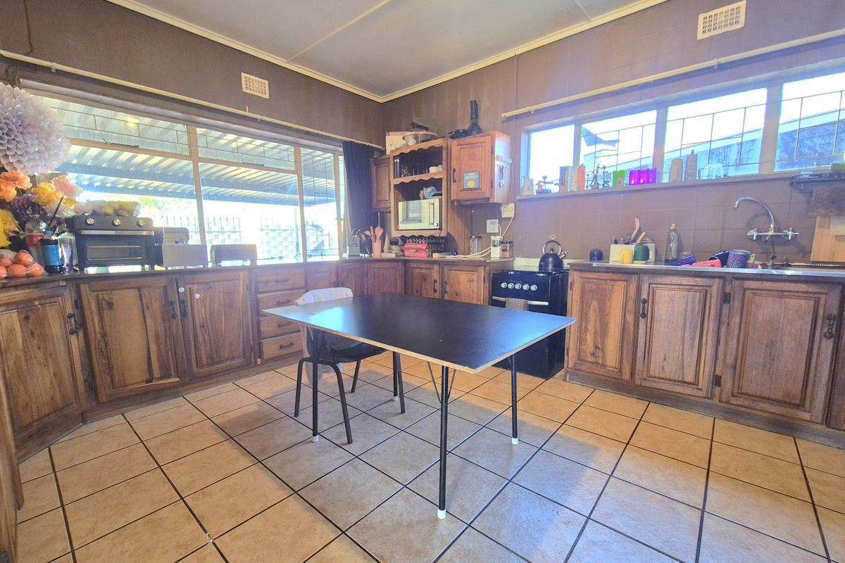 A dated kitchen featuring timber cabinetry, tiled flooring, and a functional layout with a freestanding oven and stainless steel sink.