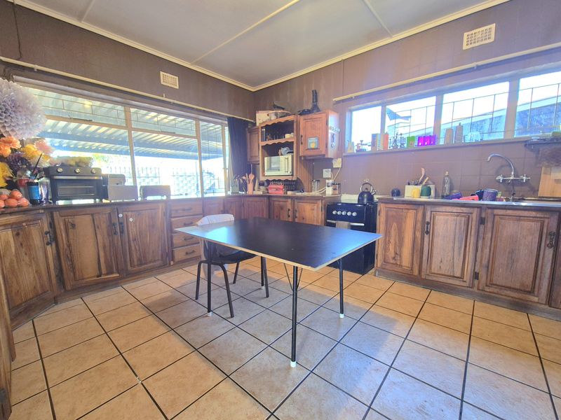 A dated kitchen featuring timber cabinetry, tiled flooring, and a functional layout with a freestanding oven and stainless steel sink.