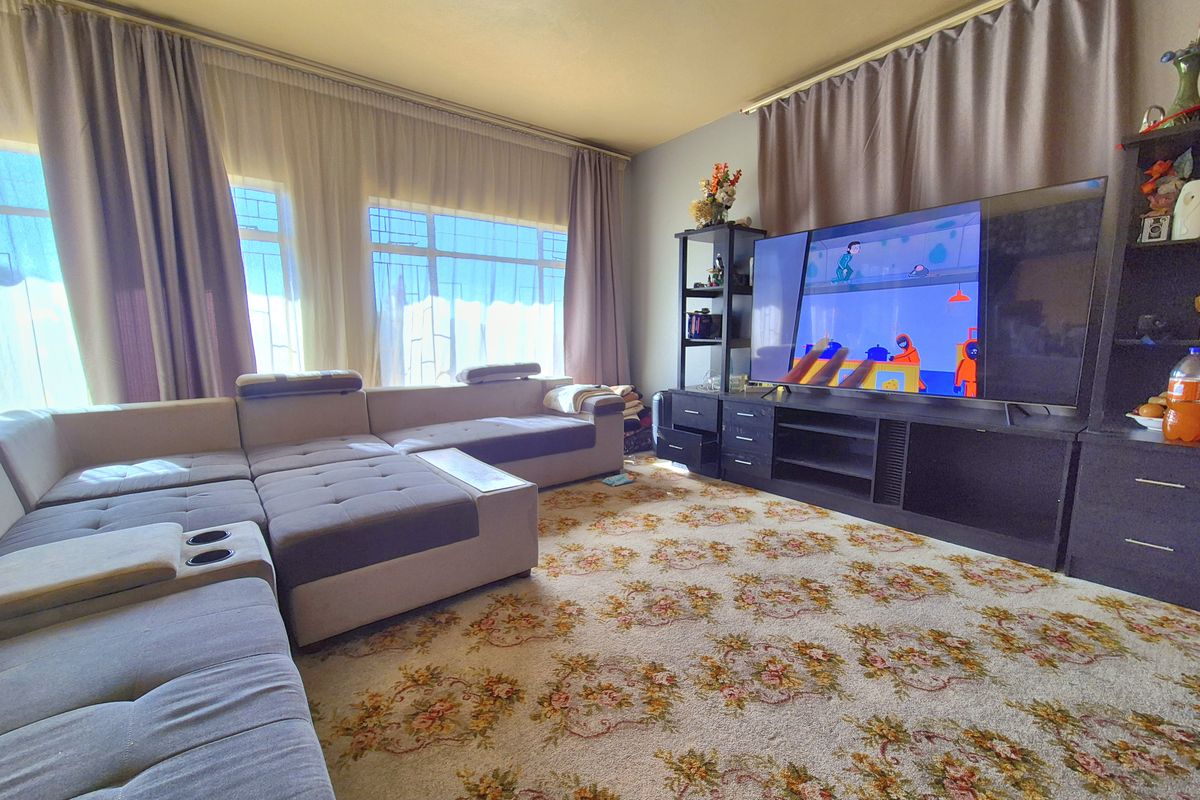 A living room featuring large windows with curtain treatments and patterned carpet flooring, offering a functional space for relaxation.