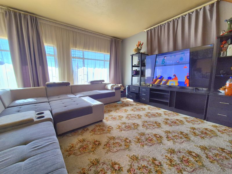 A living room featuring large windows with curtain treatments and patterned carpet flooring, offering a functional space for relaxation.