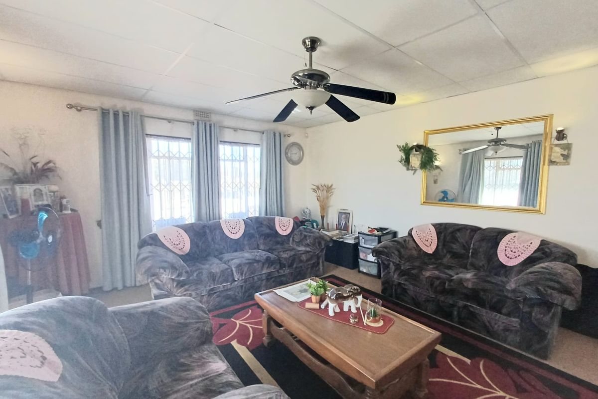A comfortable living room featuring a ceiling fan, tiled ceiling, and security bars on the windows, providing a functional and lived-in space.