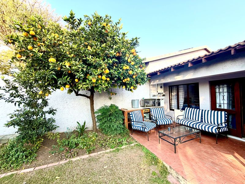 A covered brick-paved patio area adjacent to the main dwelling, featuring a mature citrus tree and direct access to the interior.