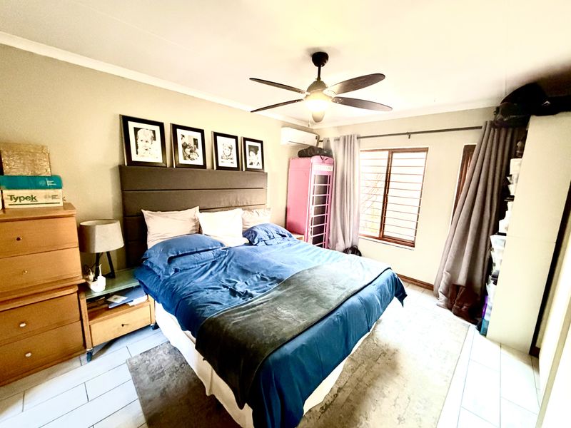 A bedroom featuring tiled flooring, a ceiling fan, and a wall-mounted air conditioning unit, providing a functional and comfortable sleeping space.
