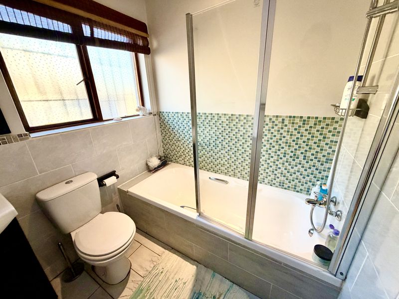 A functional bathroom featuring a bathtub with a glass shower screen, mosaic tile accents, and neutral ceramic floor tiling.