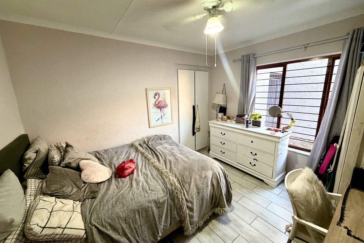 A cozy bedroom featuring tiled flooring, a ceiling fan, and a built-in cupboard, with security bars installed on the window for added peace of mind.