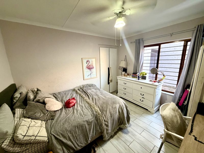 A cozy bedroom featuring tiled flooring, a ceiling fan, and a built-in cupboard, with security bars installed on the window for added peace of mind.