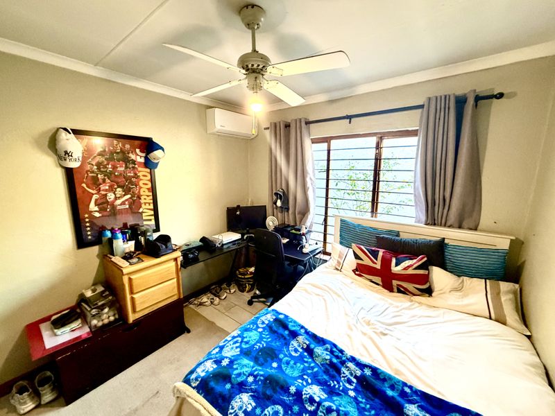 A functional bedroom featuring a ceiling fan, split-system air conditioning unit, and security bars on the window.