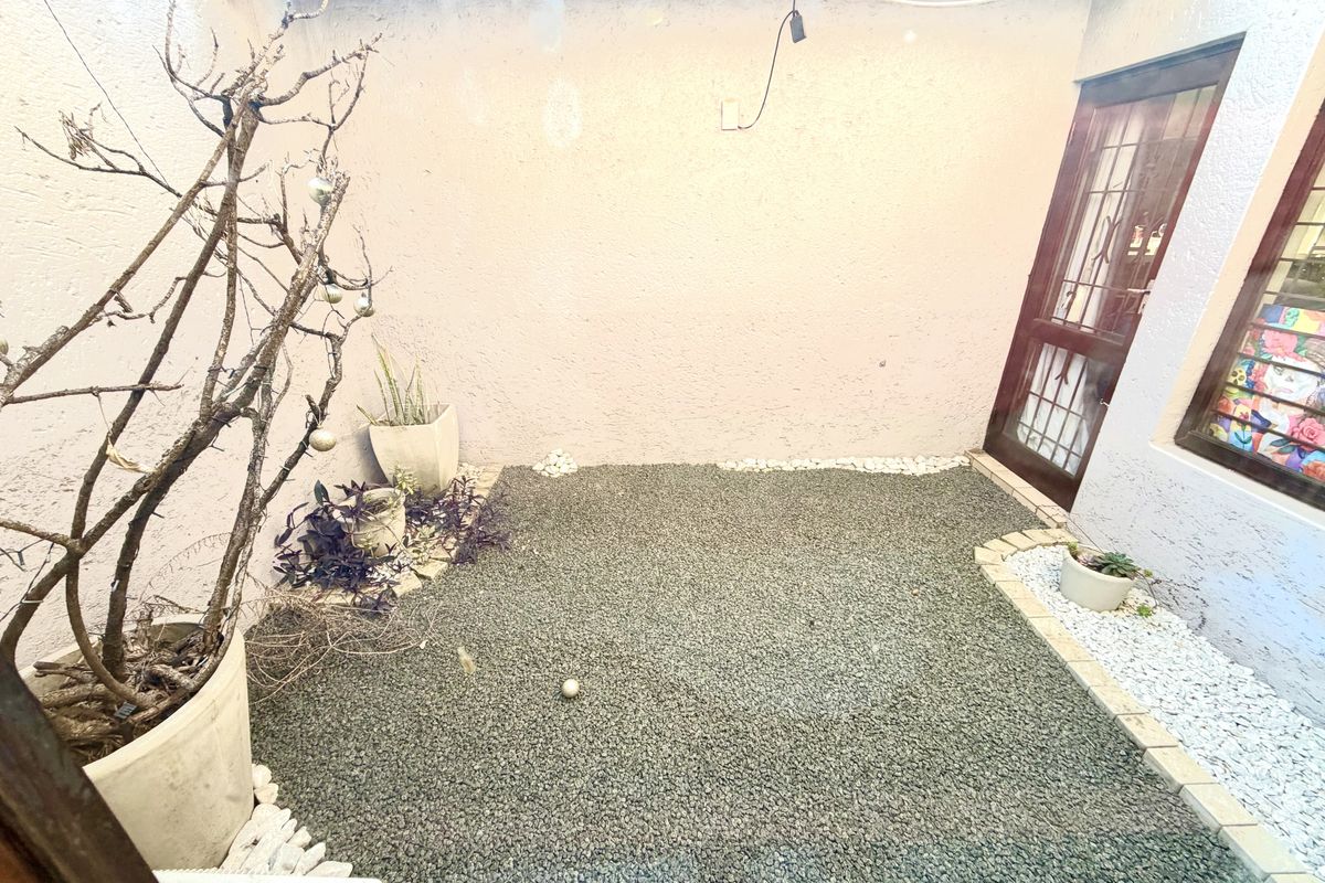 A compact, low-maintenance rear courtyard featuring a gravel surface, pebble borders, and direct access to the home via a security gate.