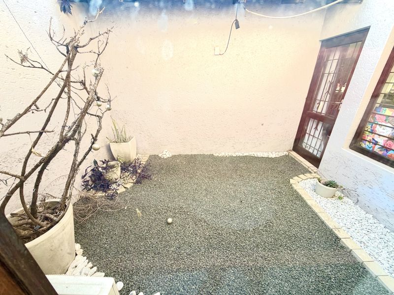 A compact, low-maintenance rear courtyard featuring a gravel surface, pebble borders, and direct access to the home via a security gate.