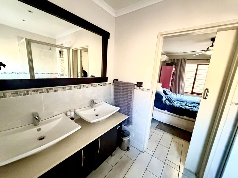 A modern bathroom featuring a double vanity with vessel sinks, tiled splashback, and a large framed mirror, with direct access to an adjacent bedroom.