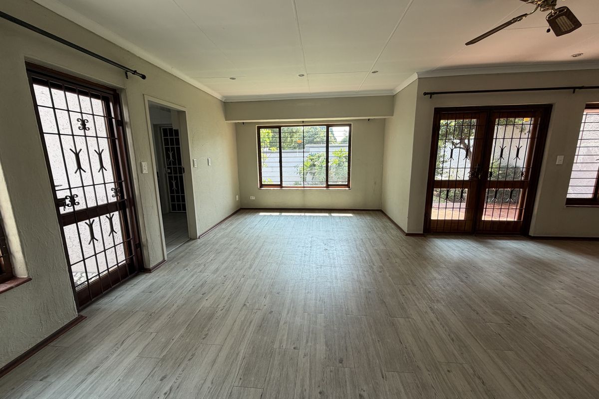 Spacious, empty living area featuring light-toned laminate flooring, a ceiling fan, and multiple access points with security gates leading to the exterior.