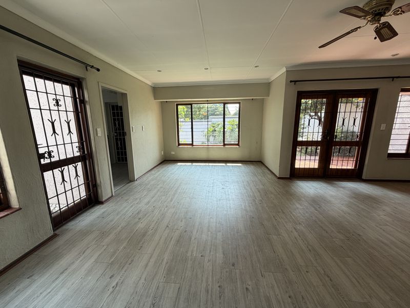 Spacious, empty living area featuring light-toned laminate flooring, a ceiling fan, and multiple access points with security gates leading to the exterior.