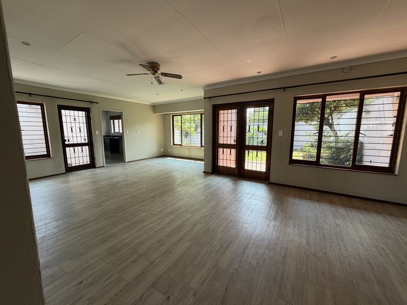 Spacious, light-filled living area featuring wood-look tile flooring, ceiling fan, and multiple access points with security gates leading to the exterior.