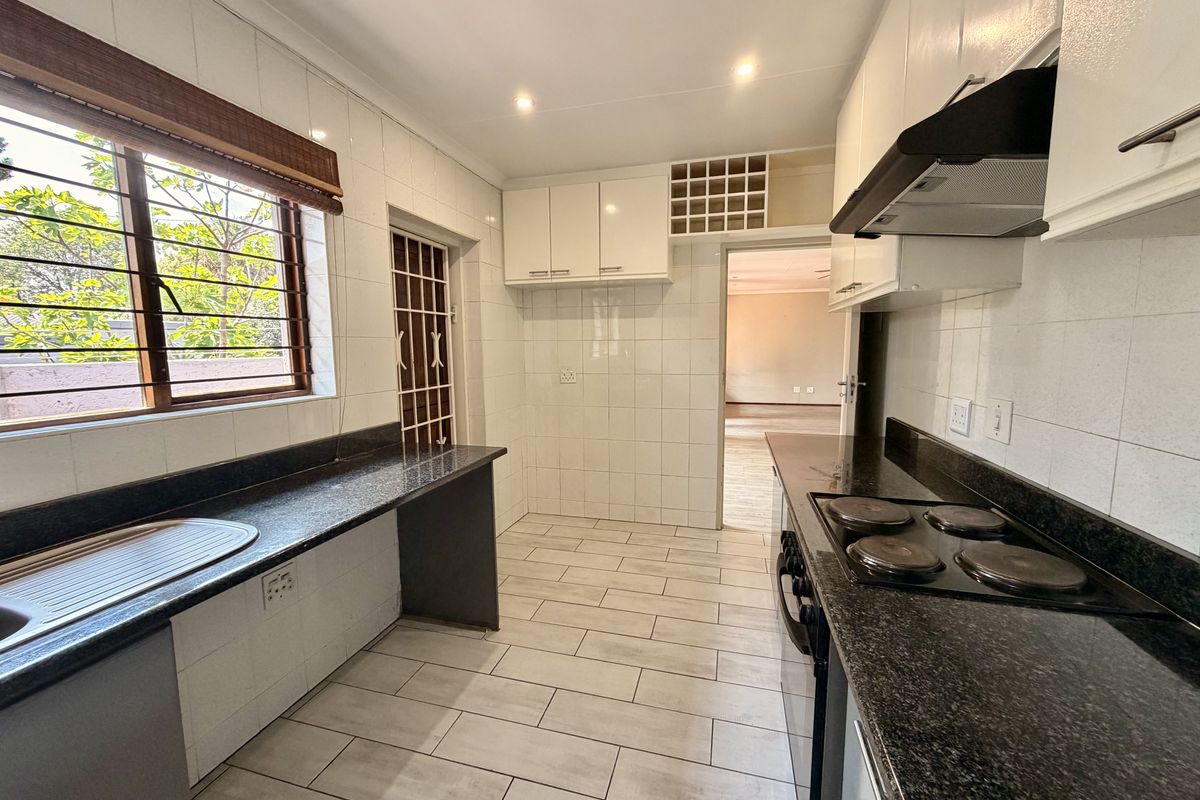 A clean, functional kitchen featuring granite countertops, built-in cabinetry, an electric hob with extractor fan, and tiled flooring with direct access to the living area.