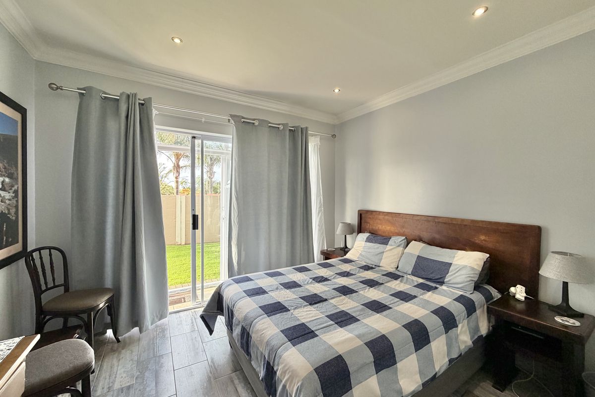 A well-lit bedroom featuring tiled flooring, recessed downlights, and a sliding glass door providing direct access to the garden.