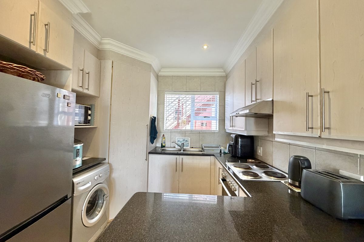 A functional kitchen featuring light-toned cabinetry, dark granite countertops, a built-in electric hob, oven, and extractor fan with a tiled backsplash.