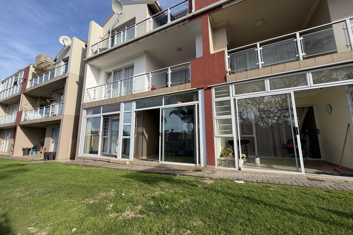Rear view of a multi-story apartment complex featuring ground-floor paved patios with sliding glass doors and upper-level balconies with glass balustrades.