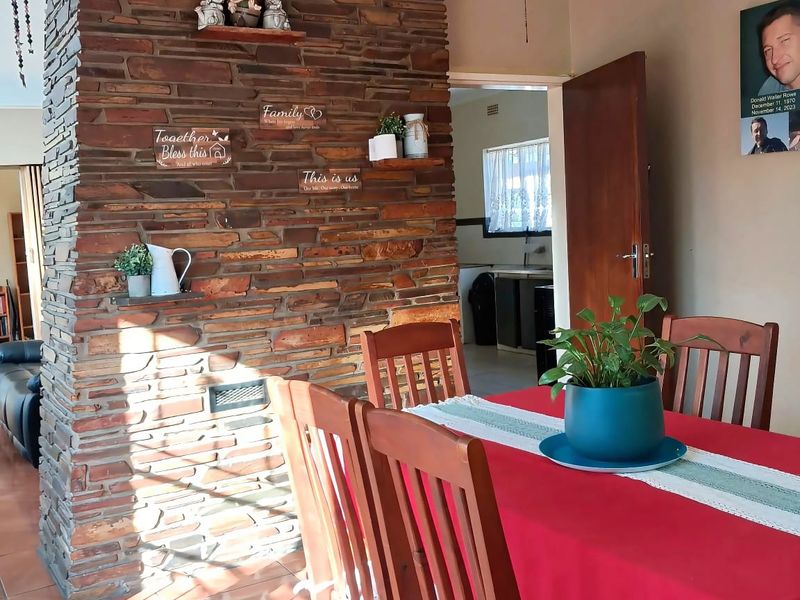 Dining room featuring a prominent stone feature wall, tiled flooring, and a ceiling fan, with an open transition to the kitchen area.
