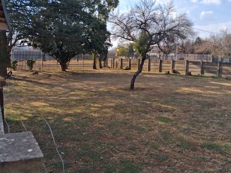 A spacious backyard featuring a large lawn, mature trees, and secure perimeter boundary walls and fencing.