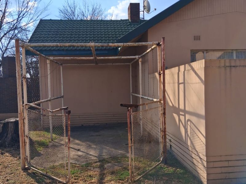 Rear exterior view of the property featuring a concrete patio area with a weathered metal frame structure and chimney.