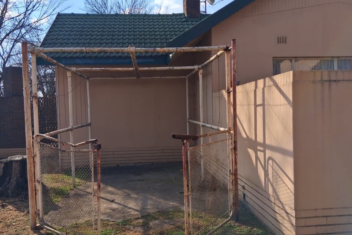 Rear exterior view of the property featuring a concrete patio area with a weathered metal frame structure and chimney.