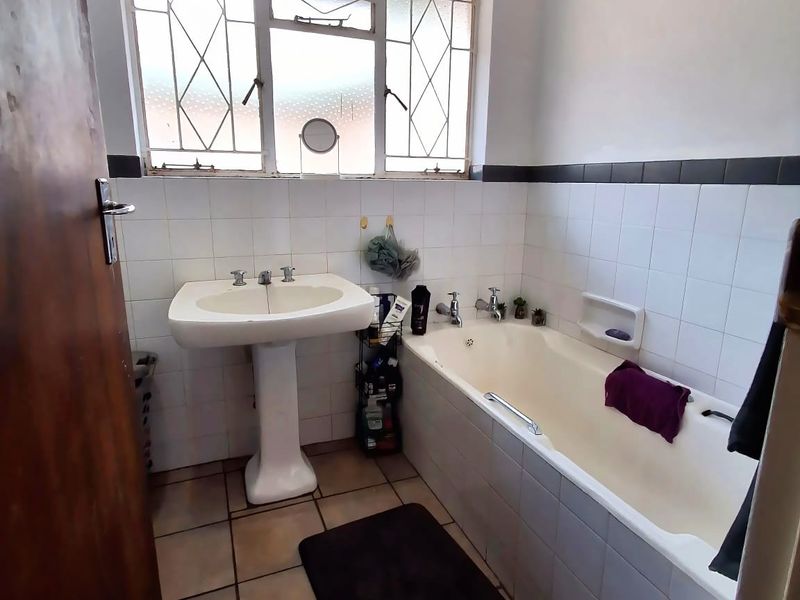 A functional bathroom featuring a pedestal basin, built-in bathtub, and tiled finishes, offering potential for a modern renovation.