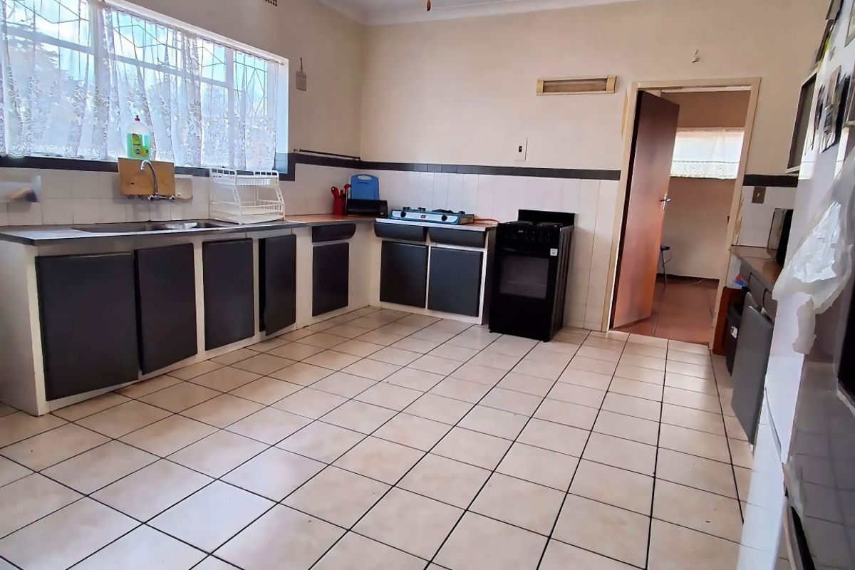 A functional kitchen featuring tiled flooring, built-in cabinetry, a stainless steel sink, and a freestanding oven, offering potential for modernization.