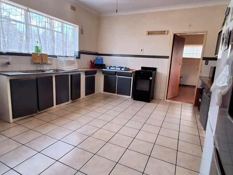 A functional kitchen featuring tiled flooring, built-in cabinetry, a stainless steel sink, and a freestanding oven, offering potential for modernization.