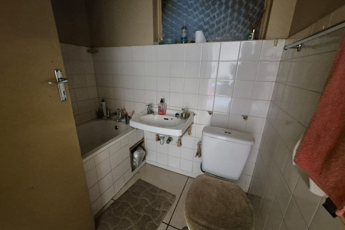 A dated bathroom featuring a built-in bathtub, wall-mounted basin, and toilet, requiring significant renovation and cosmetic updates to improve its condition and functionality.