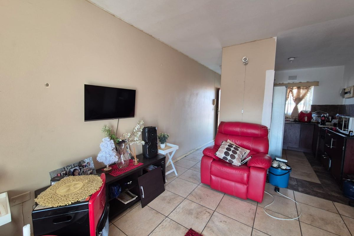 Open-plan living area featuring tiled flooring and a transition into the kitchen space, requiring cosmetic updates to walls and finishes.