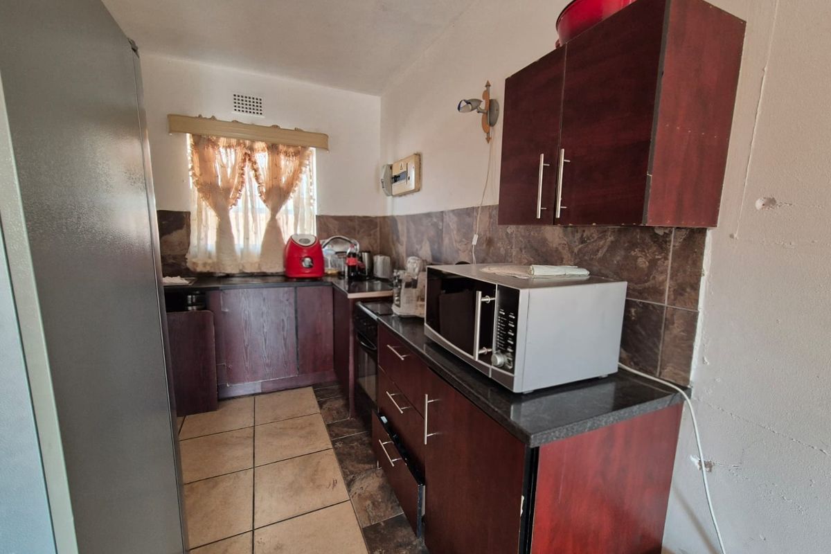 A compact kitchen featuring dark wood cabinetry, granite countertops, and tiled backsplash, requiring some cosmetic updates to improve its overall appeal.