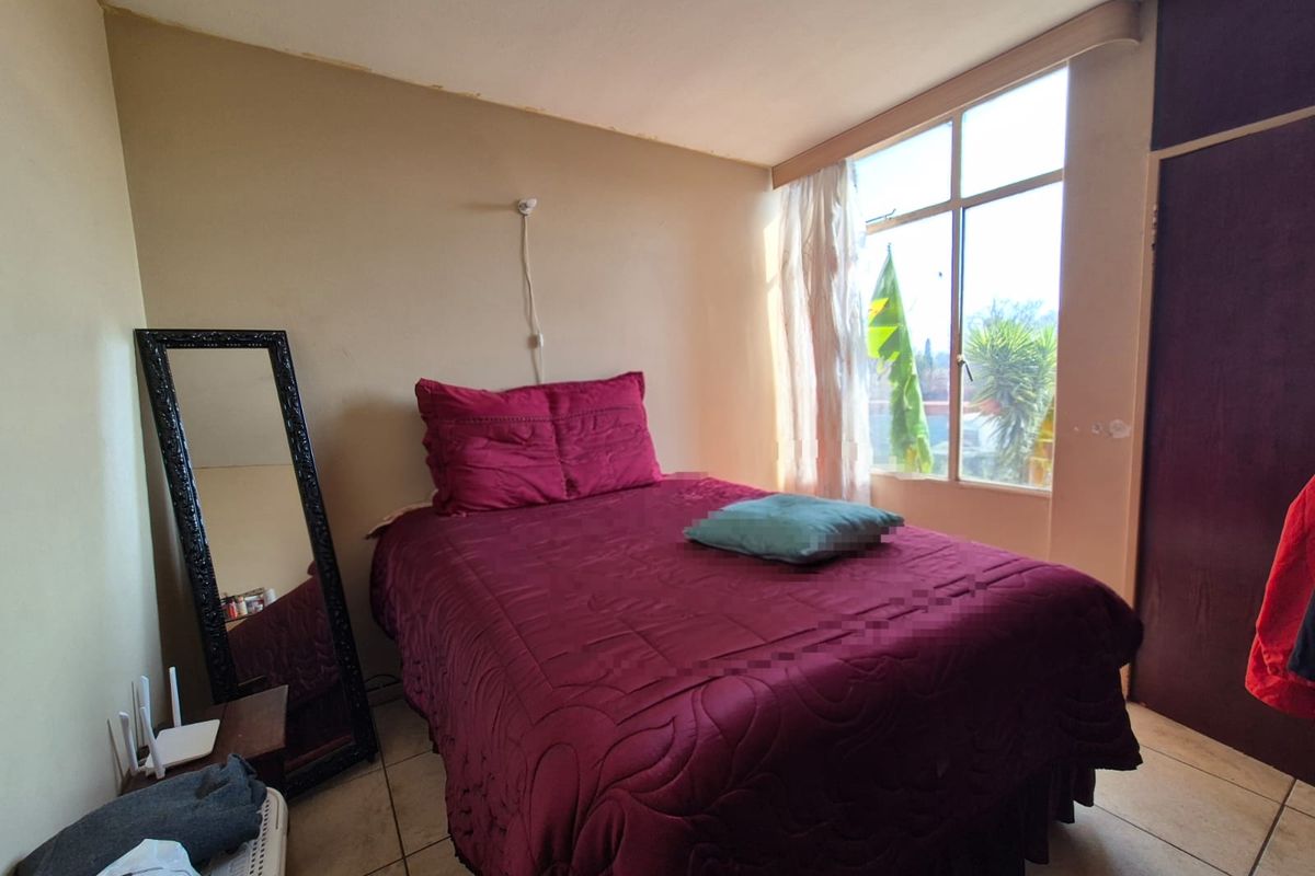 A bedroom featuring tiled flooring, a built-in cupboard, and a large window providing natural light. The room requires cosmetic updates to the walls.