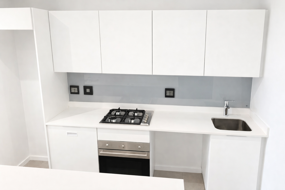 A modern, minimalist kitchen featuring white cabinetry, stone countertops, a built-in gas hob, oven, and a sleek glass splashback.
