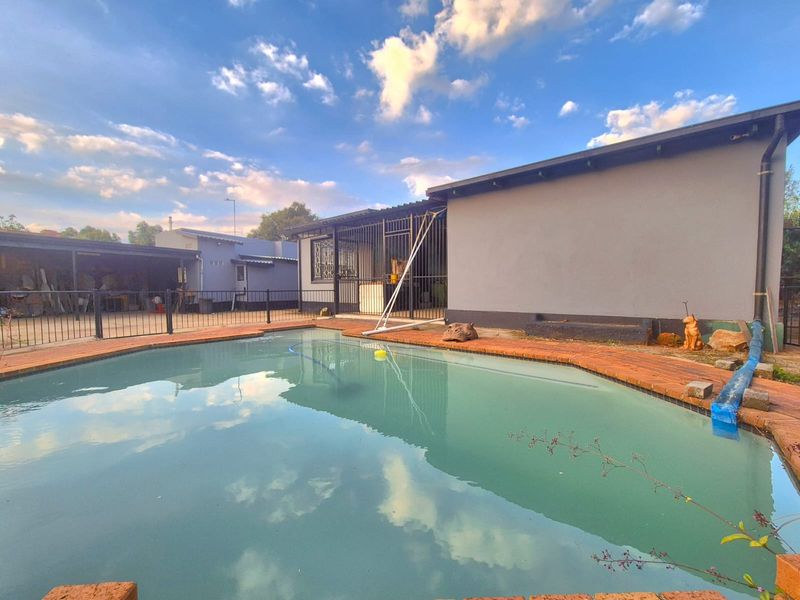 Outdoor pool area featuring a swimming pool with brick coping, metal security fencing, and adjacent exterior building wall.