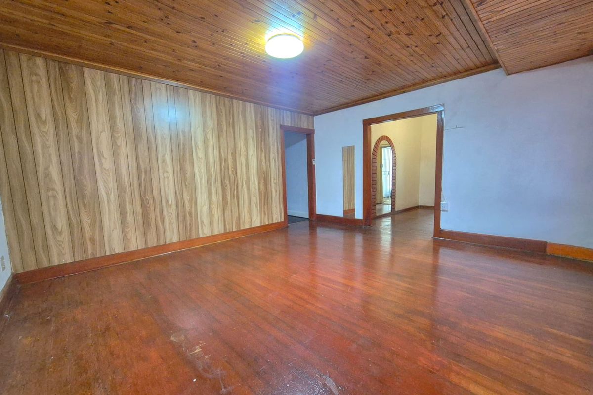 An empty living room featuring timber ceiling paneling, wood-paneled walls, and hardwood flooring, with an arched doorway leading to an adjacent space.