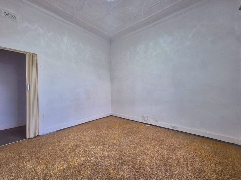 An empty bedroom featuring a classic pressed metal ceiling, carpeted flooring, and a folding door, offering a blank canvas for renovation.