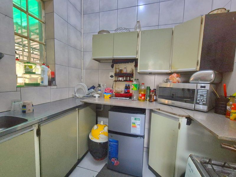 A compact kitchen featuring dated built-in cabinetry, laminate countertops, tiled walls, and a stainless steel sink, offering potential for modernization.