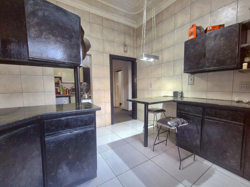 A dated kitchen featuring dark built-in cabinetry, tiled walls and flooring, and a breakfast bar area with pendant lighting.