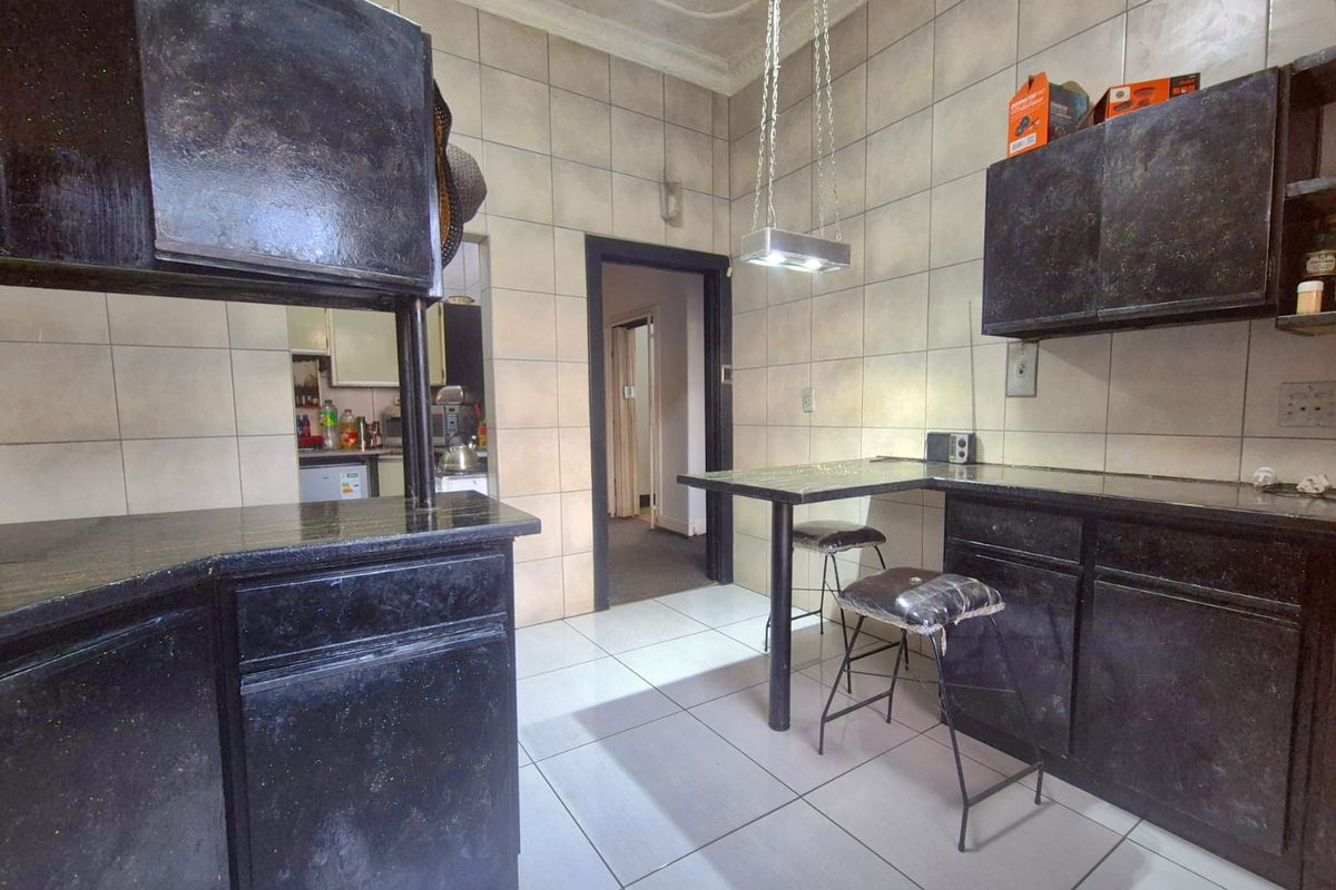A dated kitchen featuring dark built-in cabinetry, tiled walls and flooring, and a breakfast bar area with pendant lighting.