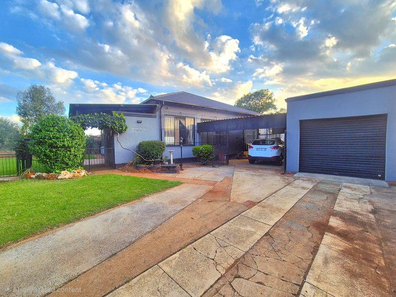 Front exterior view of a residential house featuring a paved driveway, attached garage, carport, and a landscaped front garden area.