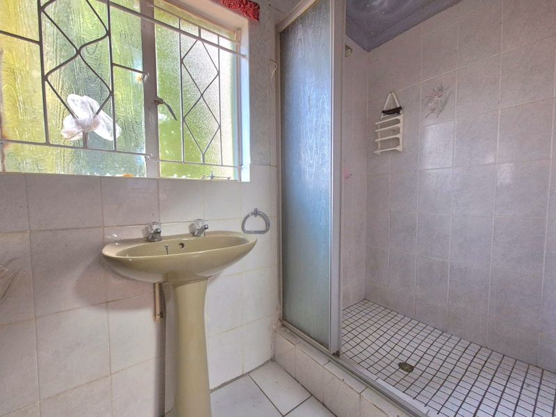 A dated bathroom featuring a pedestal basin, a shower enclosure with a glass door, and tiled finishes throughout.